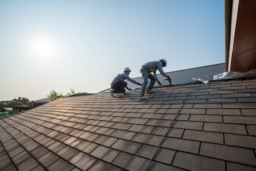 Roofing professionals installing shingles on a residential roof under a clear blue sky, showcasing quality craftsmanship in home restoration and roofing services.